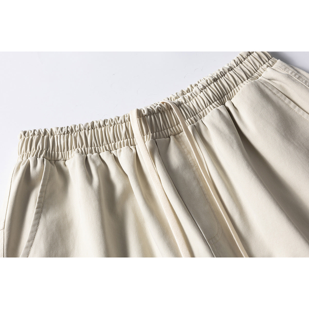 Close-up of cream shorts showing the gathered elastic waistband, drawstring, and front pocket seam.
