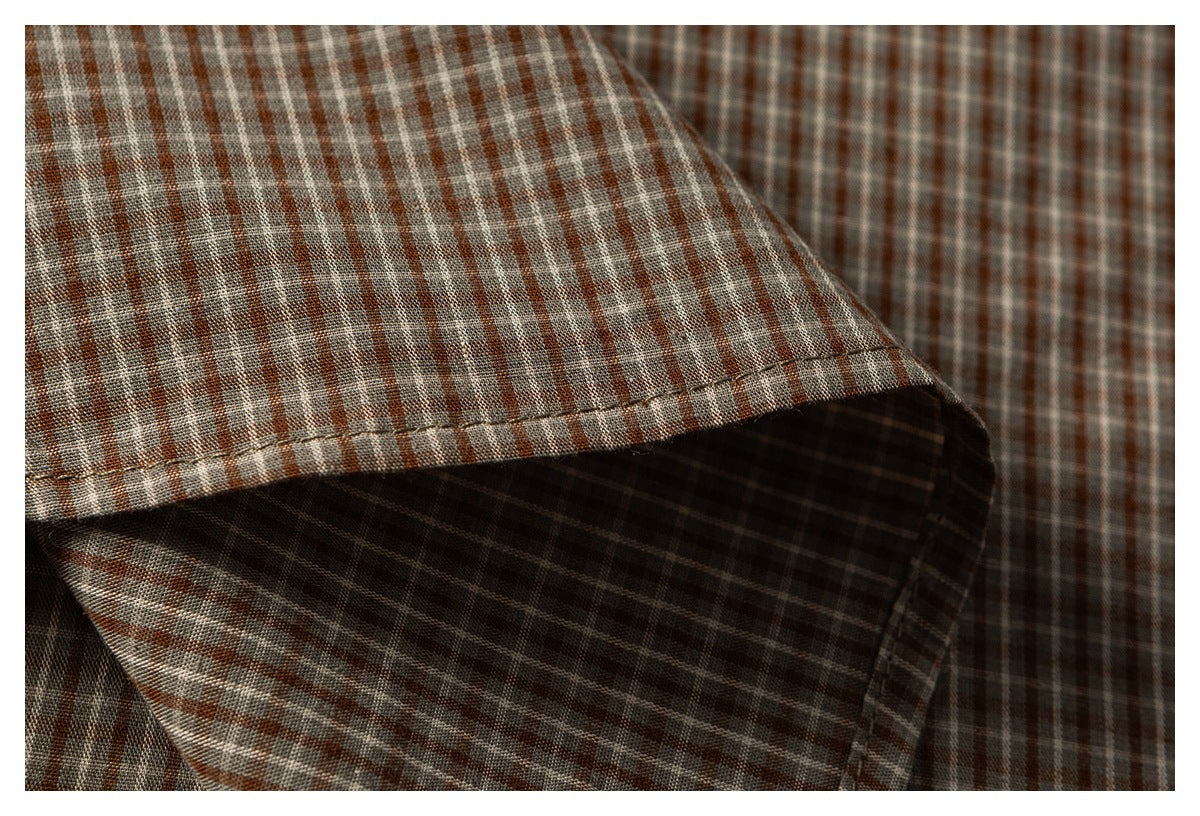 Close-up of brown, gray, and cream plaid fabric with a folded, stitched edge and visible woven pattern.