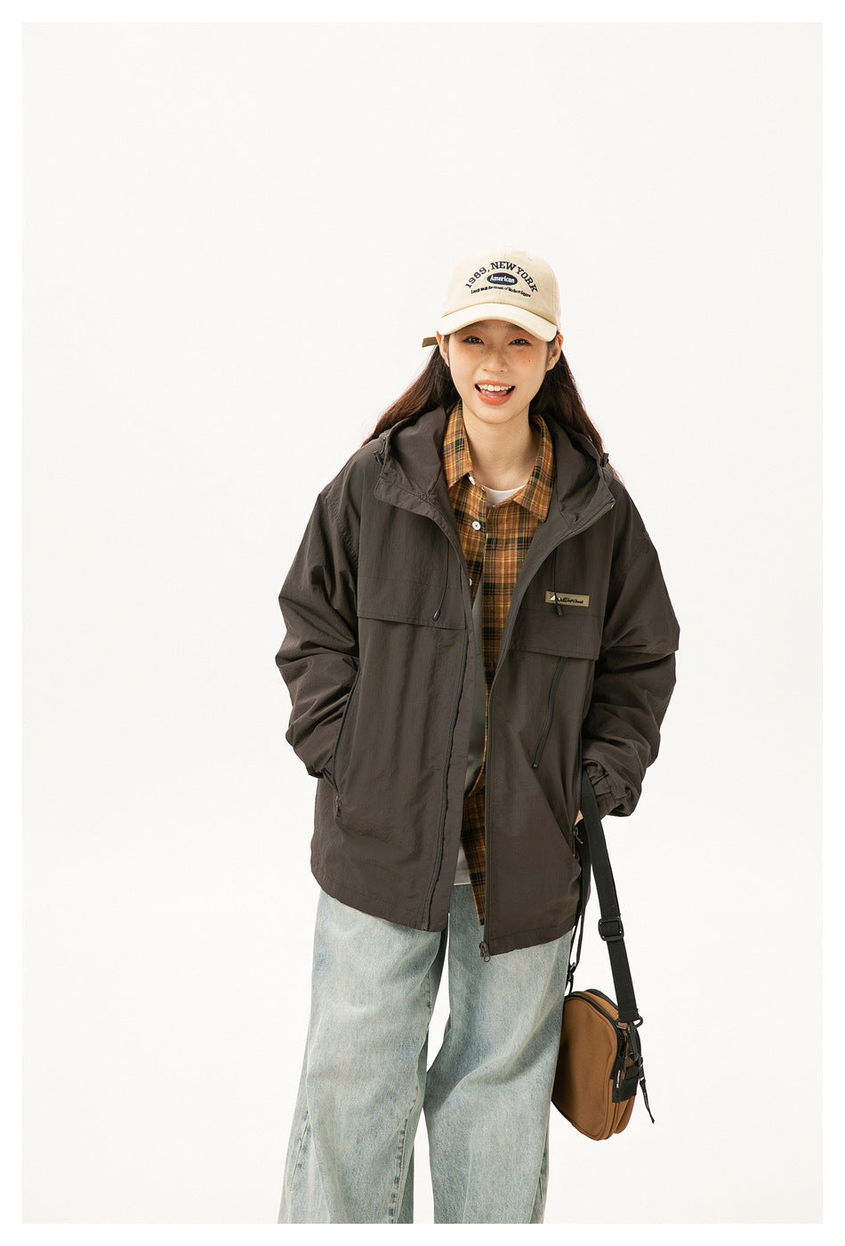Woman wearing a dark brown hooded jacket over a plaid shirt and loose jeans, shown from head to mid-calf.