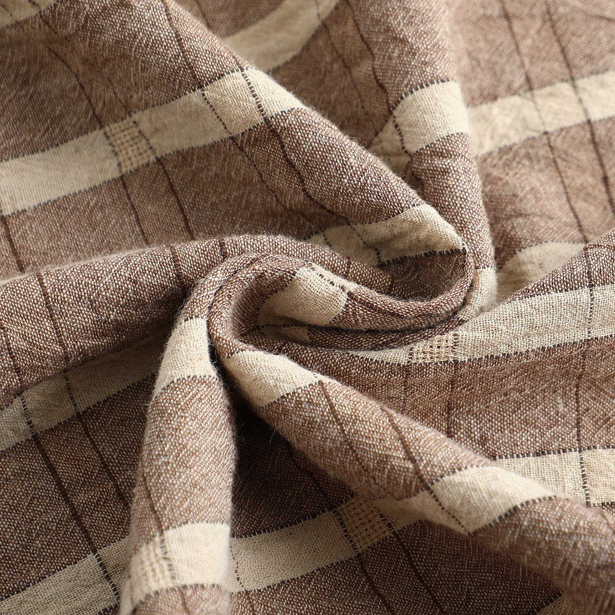 Close-up of loosely folded brown and cream plaid fabric showing its woven texture.