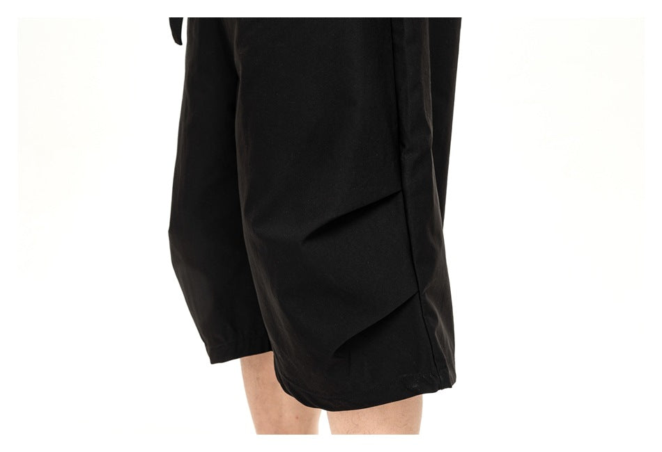 Cropped view of a person wearing black, wide-leg knee-length shorts, showing the side and hem.