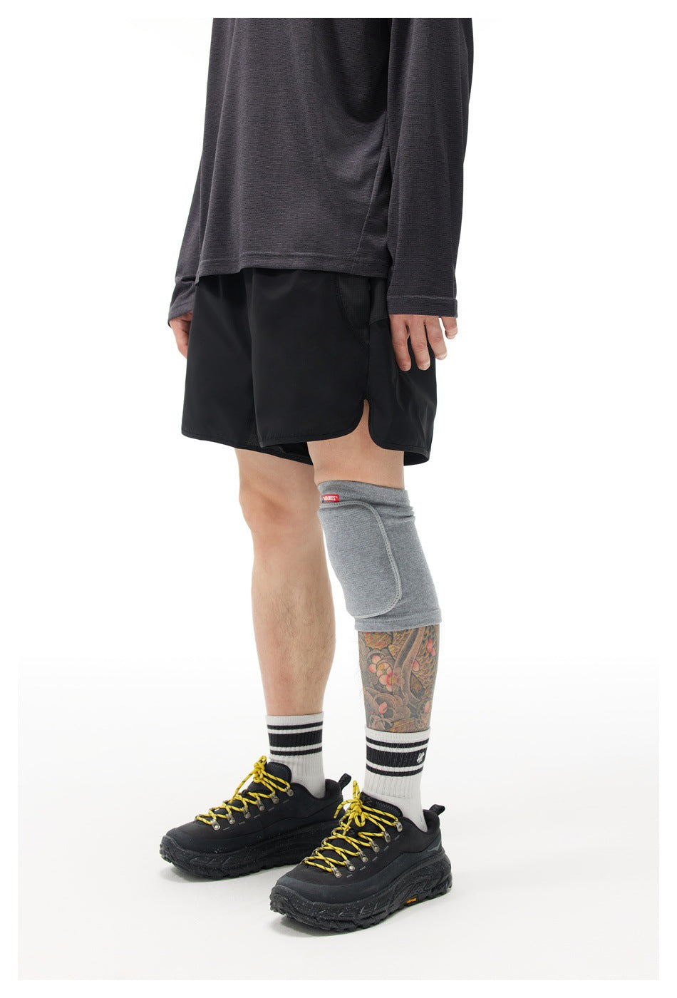 Side view of a model wearing black athletic shorts with curved hems and a dark long-sleeve shirt.