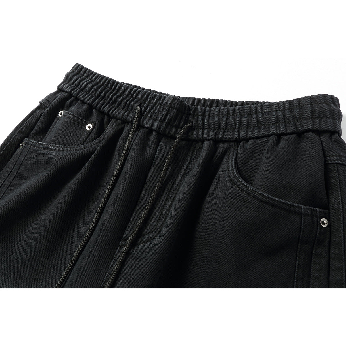 Close-up of black jogger-style pants showing an elastic waistband, drawstrings, front pockets and metal rivets.