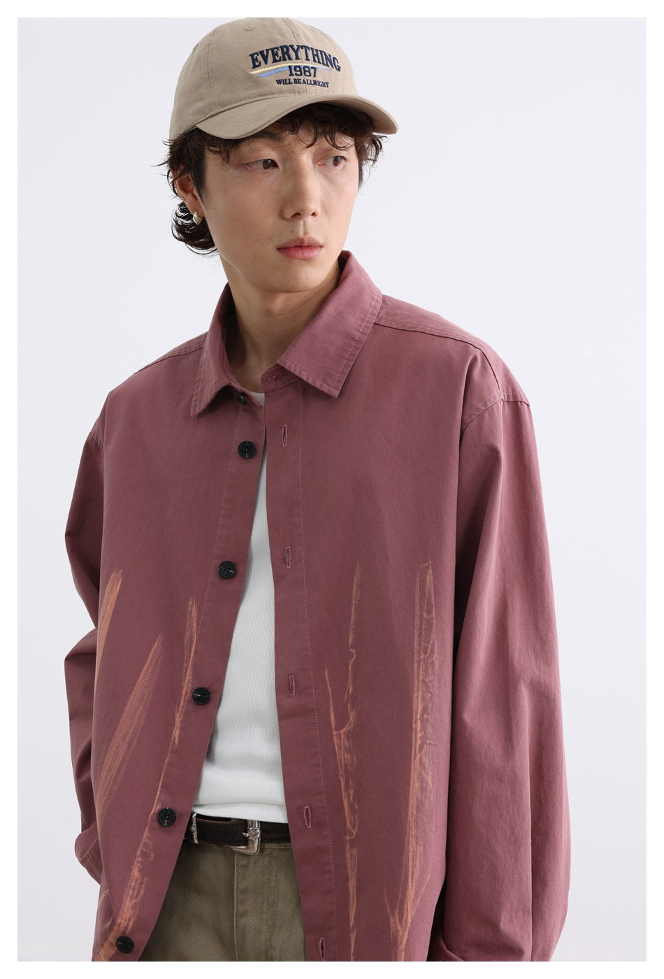 Close view of a model wearing a dusty rose button-up shirt with tan brushstroke graphics and a beige cap.