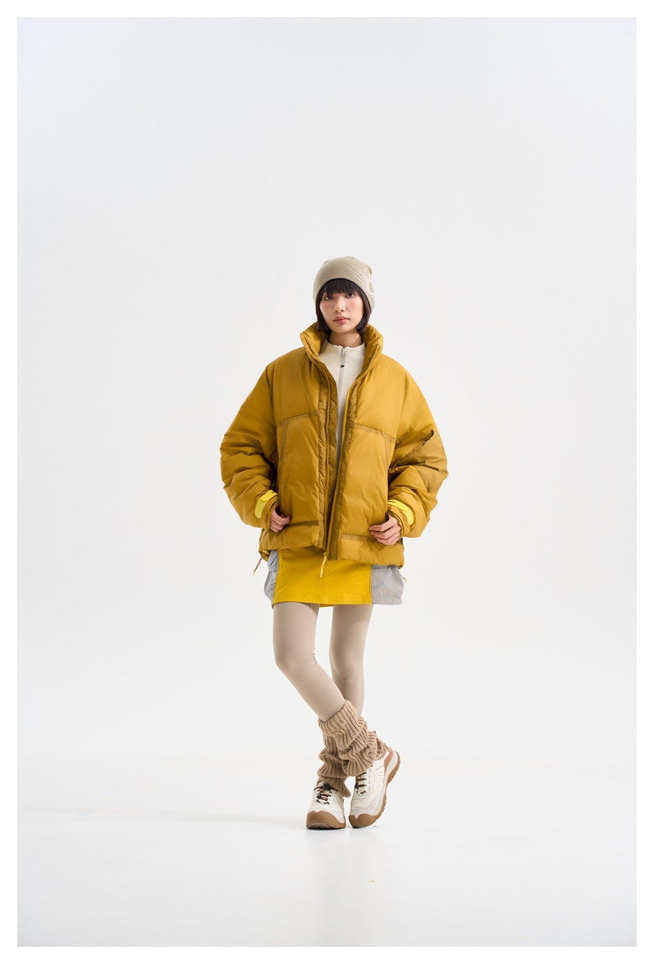 Model wearing an open mustard-yellow padded jacket over a white top, shown from the front.