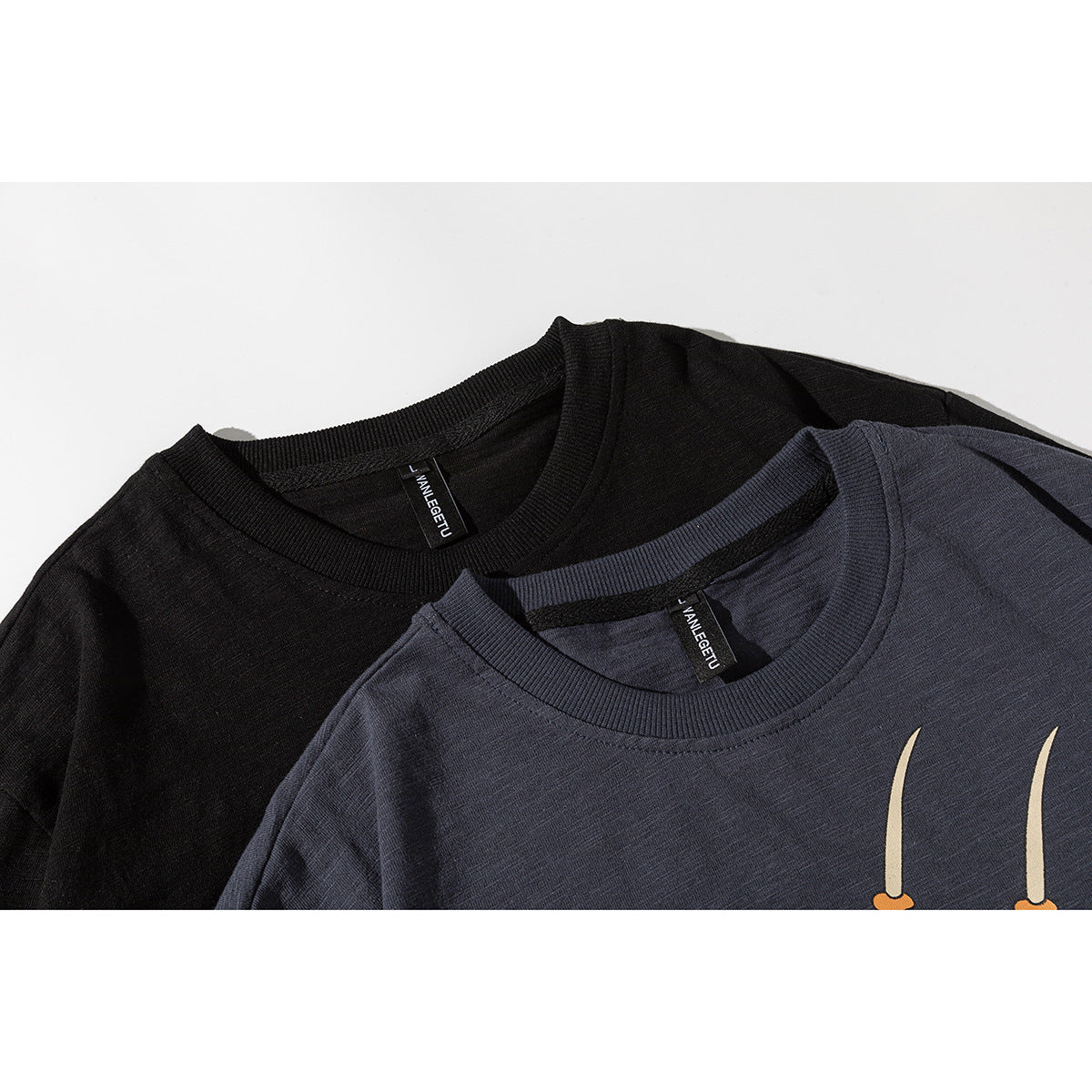 Close-up of black and charcoal T-shirts showing ribbed crew necks and partial cream-and-orange graphics.