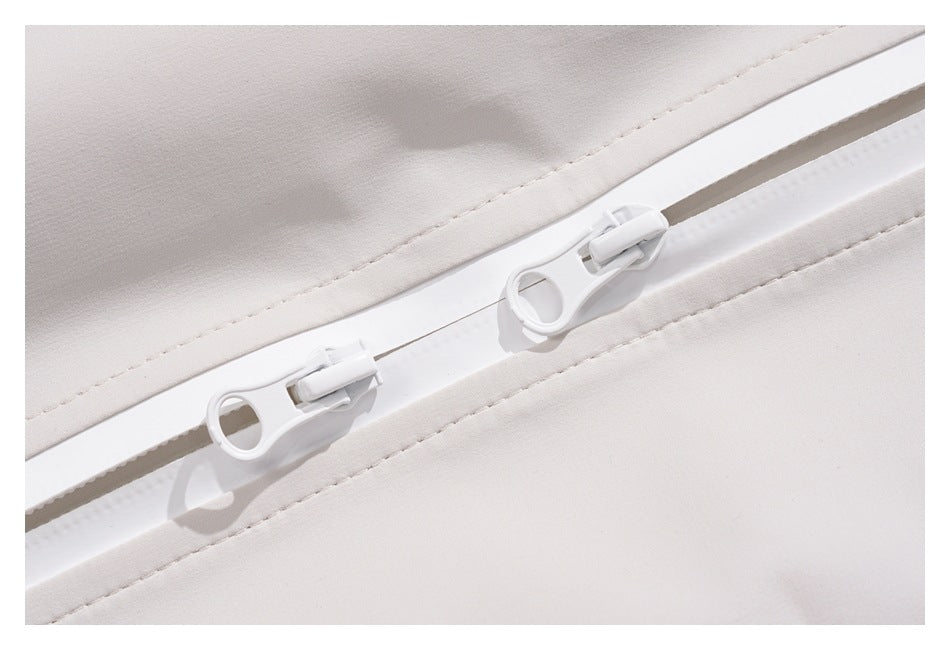 Close-up of two white zipper pulls on a white garment with stitched seams.