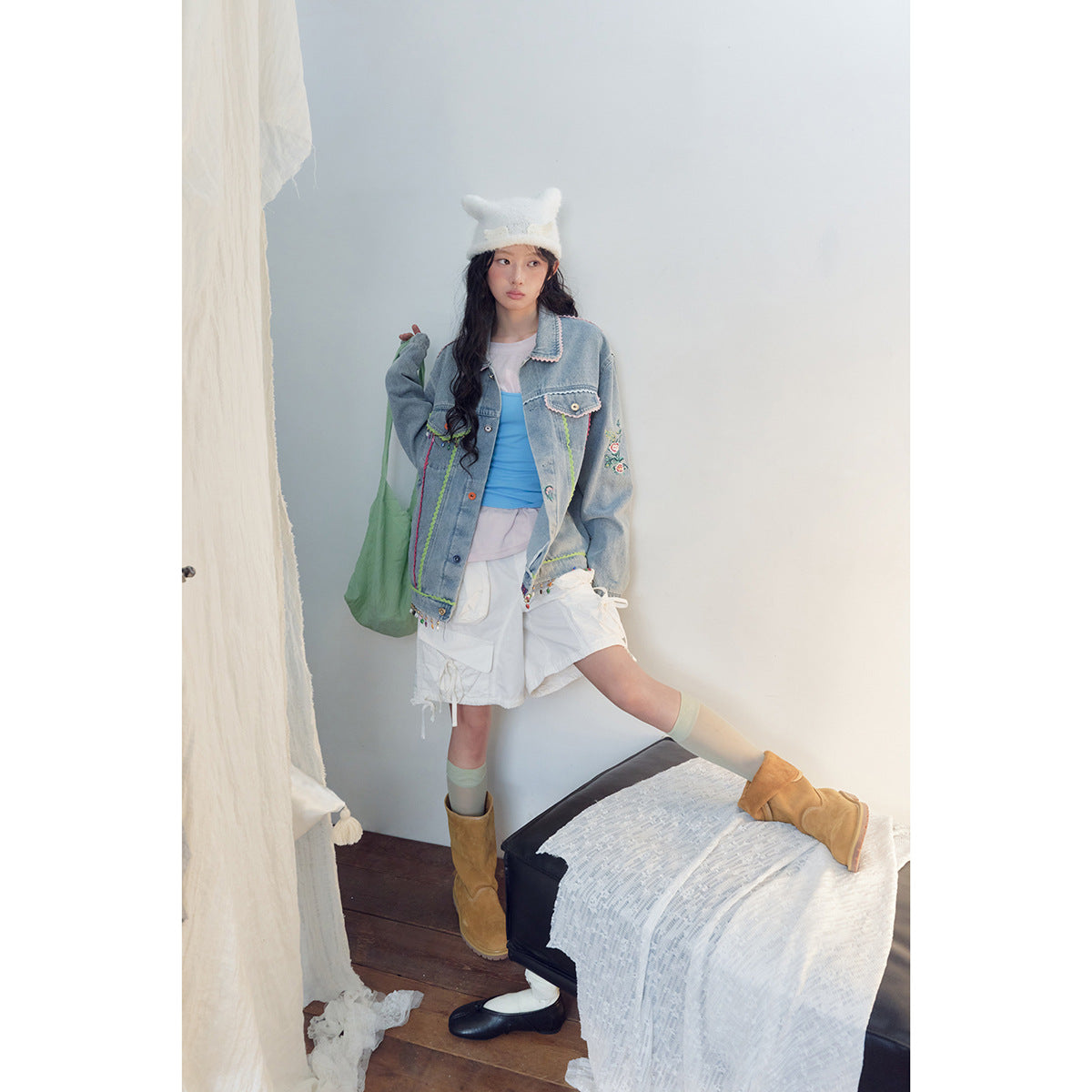Model wearing an embellished light-wash denim jacket with white cargo shorts, a blue top, and tan boots.