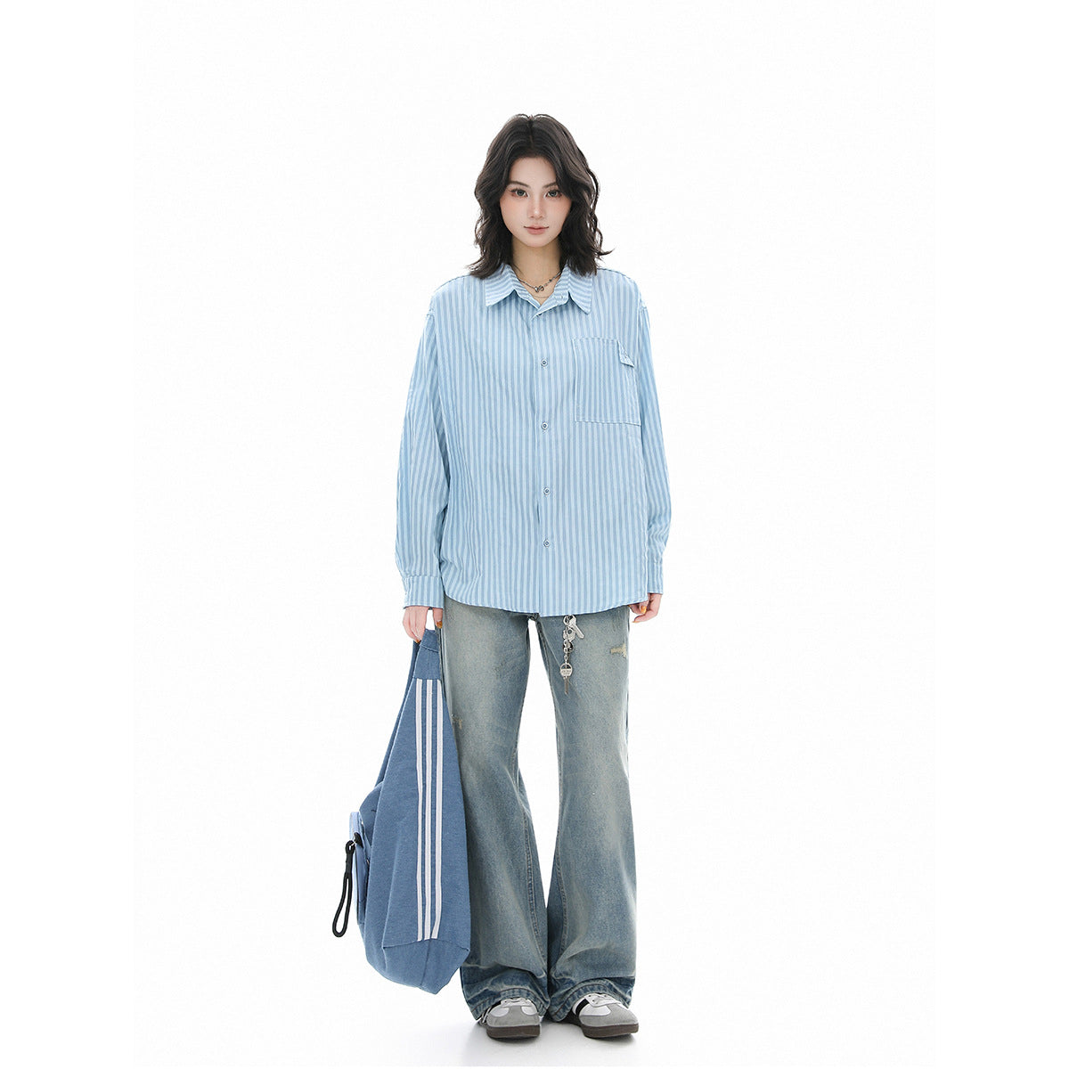 Full-length front view of a model in a light blue striped button-up shirt and loose gray jeans.