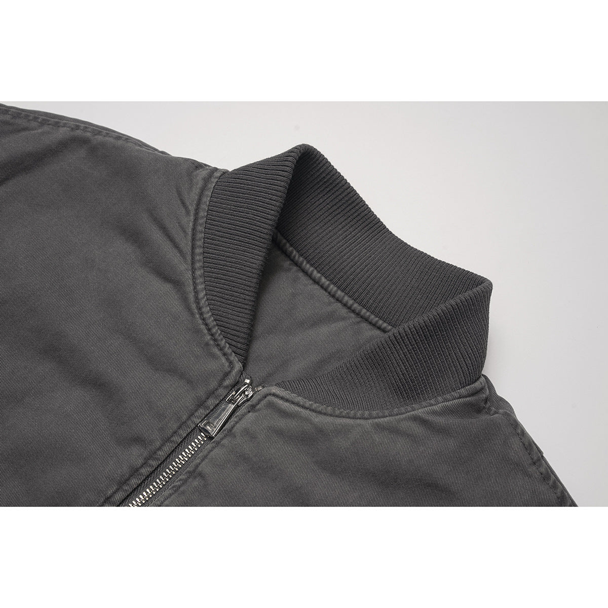 Close-up of a charcoal bomber jacket's ribbed collar and silver front zipper.