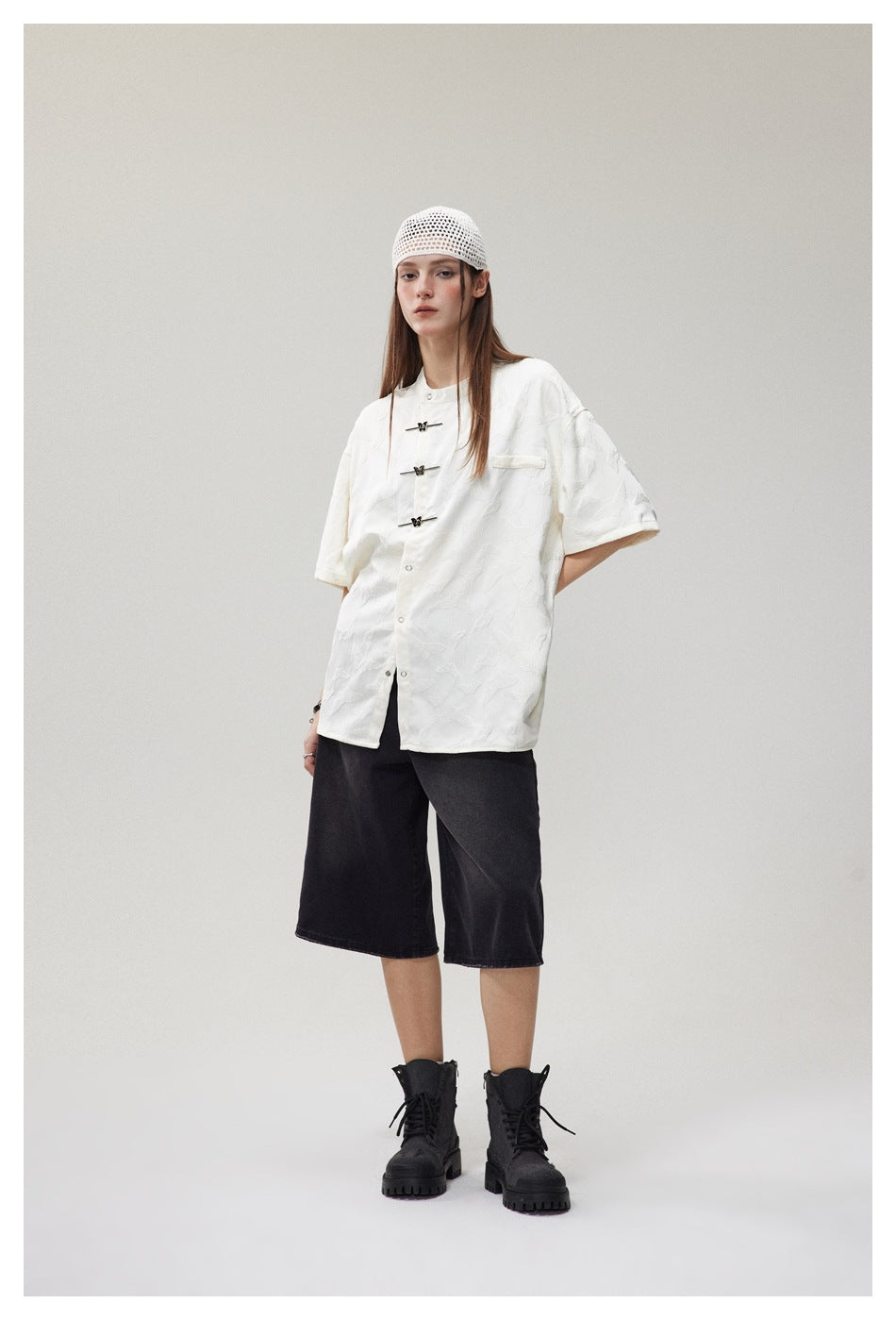 Three-quarter view of a model in an oversized white patterned shirt with frog closures and black knee-length shorts.