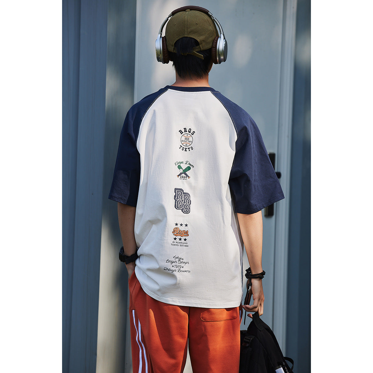 Back view of a model wearing a white T-shirt with navy raglan sleeves and several graphics down the back.