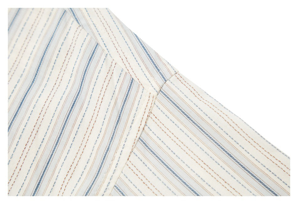Close-up of the shirt shoulder seam and ivory fabric with fine blue and brown stripes.
