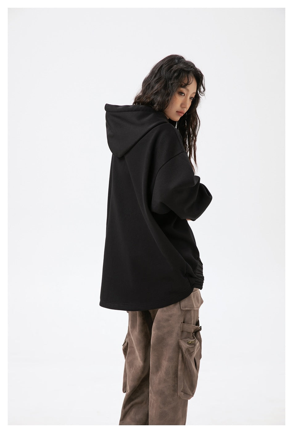 Side view of a model wearing an oversized black hoodie with a plain back and brown cargo pants.