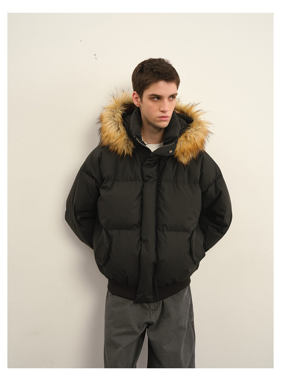 Model wearing a black hooded puffer jacket with tan fur trim and gray trousers, shown from the front.