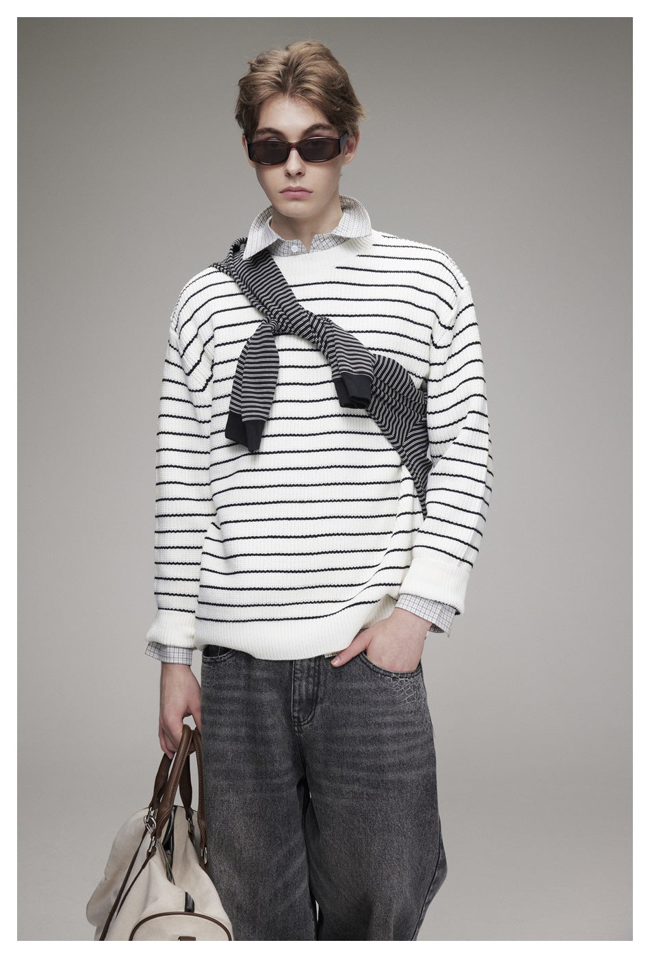 Close view of a model wearing an ivory sweater with thin black stripes and a dark striped scarf.