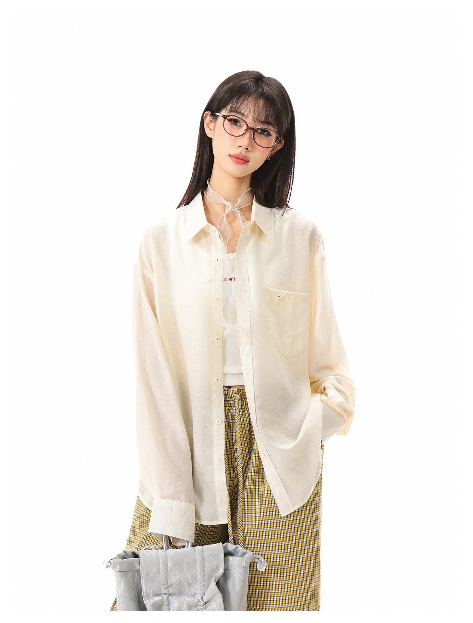 Close view of a woman in an open beige button-up shirt with chest pocket, tank top and sheer neck scarf