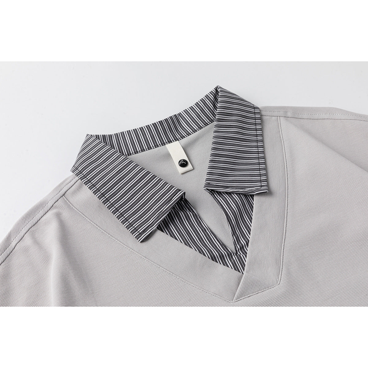 Close-up of a light gray shirt's V-neck and black-and-white striped collar.