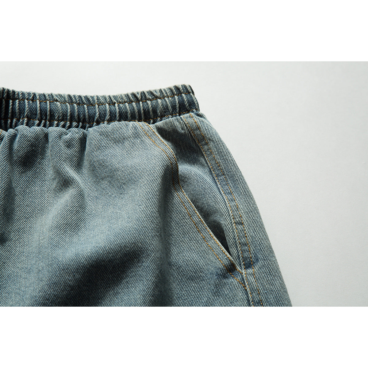 Close-up of blue-gray denim shorts showing the gathered elastic waistband and angled front pocket seam.