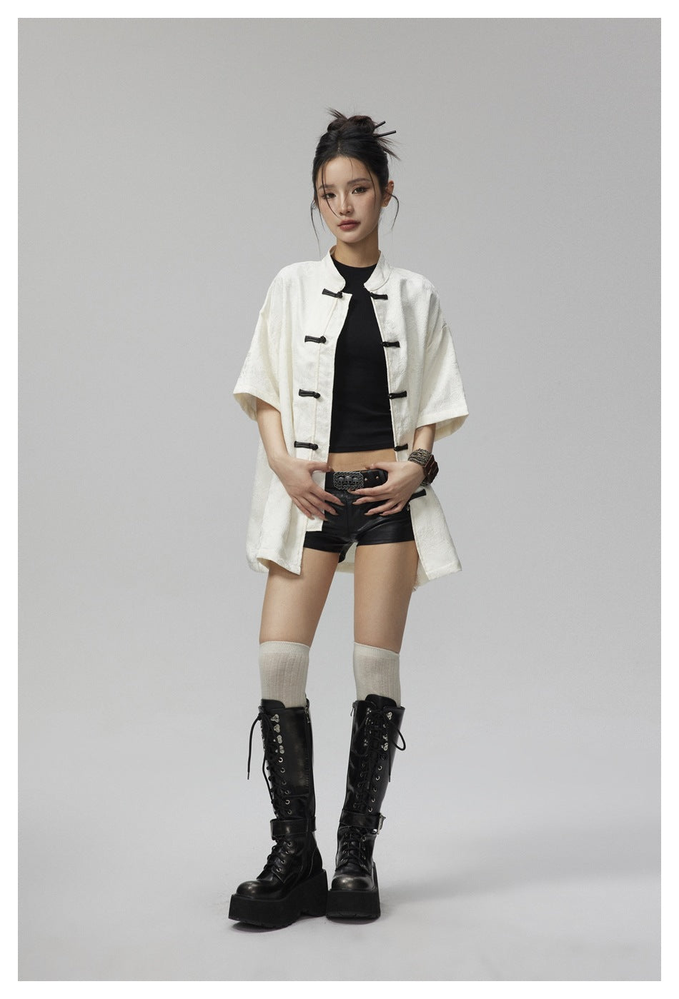 Model wearing an open off-white knot-button short-sleeve shirt over a black top, black shorts and tall black boots