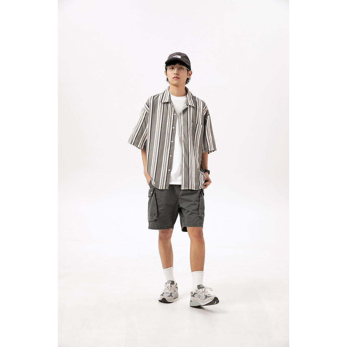 Front view of a model wearing a striped short-sleeve shirt over a white tee and dark gray cargo shorts.