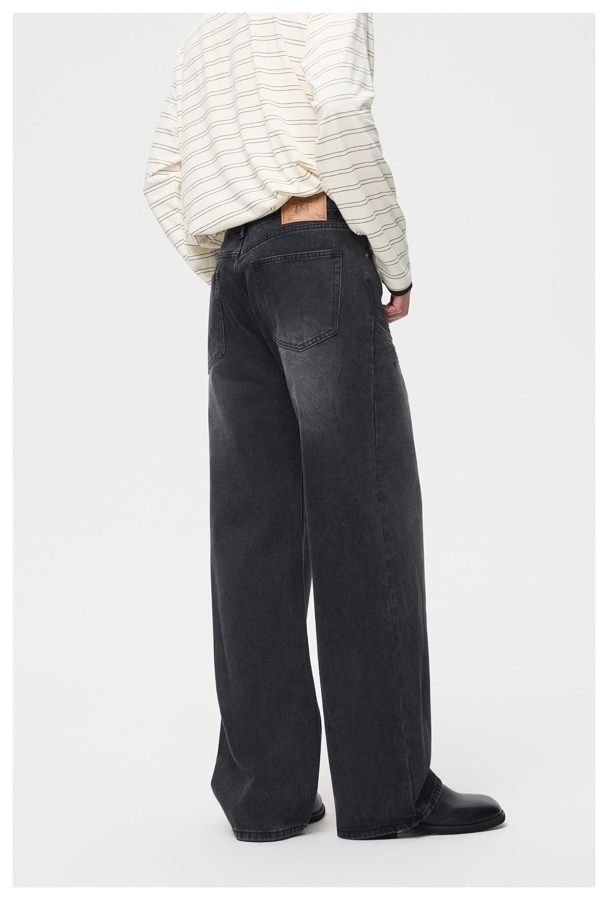 Rear view of a model wearing dark charcoal wide-leg jeans with two back pockets and a striped shirt.