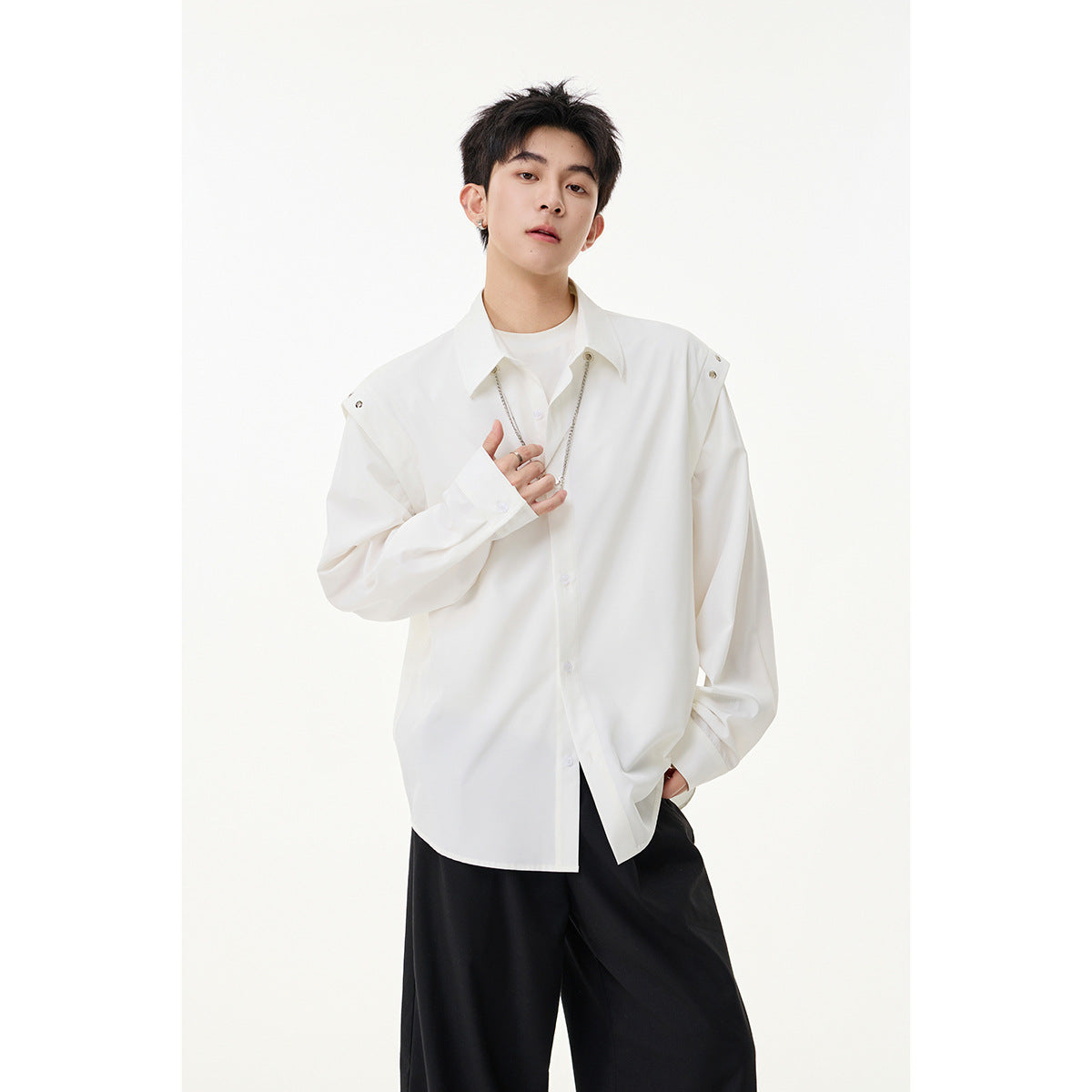 Model wearing a white oversized button-front shirt with shoulder snaps over a white tee and black trousers.