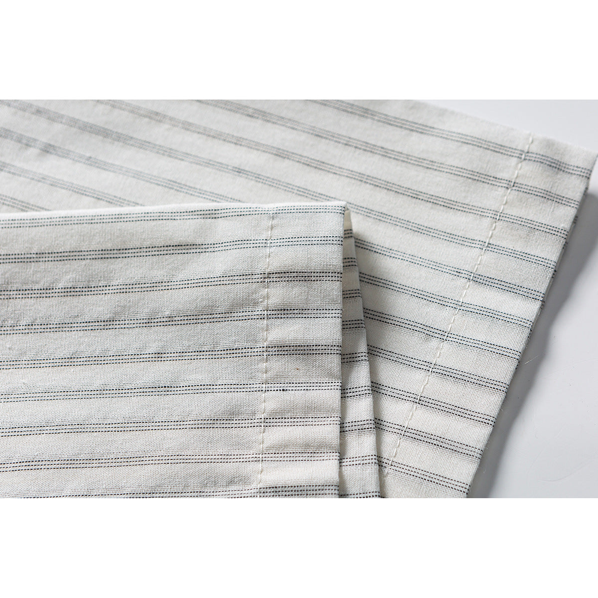Close-up of a cream shirt sleeve with fine dark horizontal stripes and a stitched cuff.