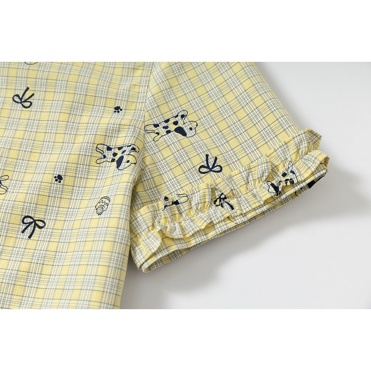 Close-up of the short sleeve with a gathered ruffle cuff on a yellow plaid shirt with navy prints.