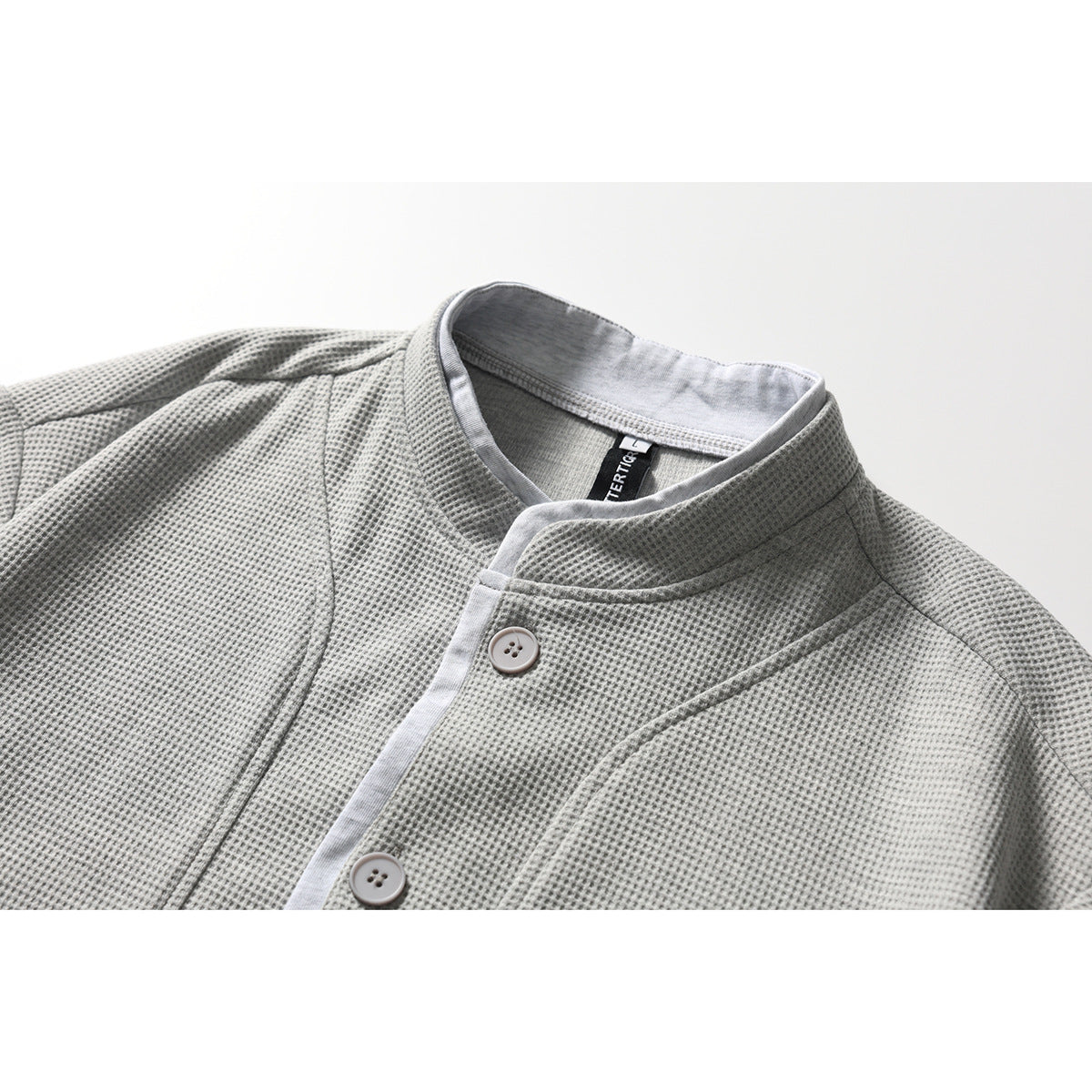 Close-up of a light gray textured jacket with a stand collar, contrasting placket, and buttons.