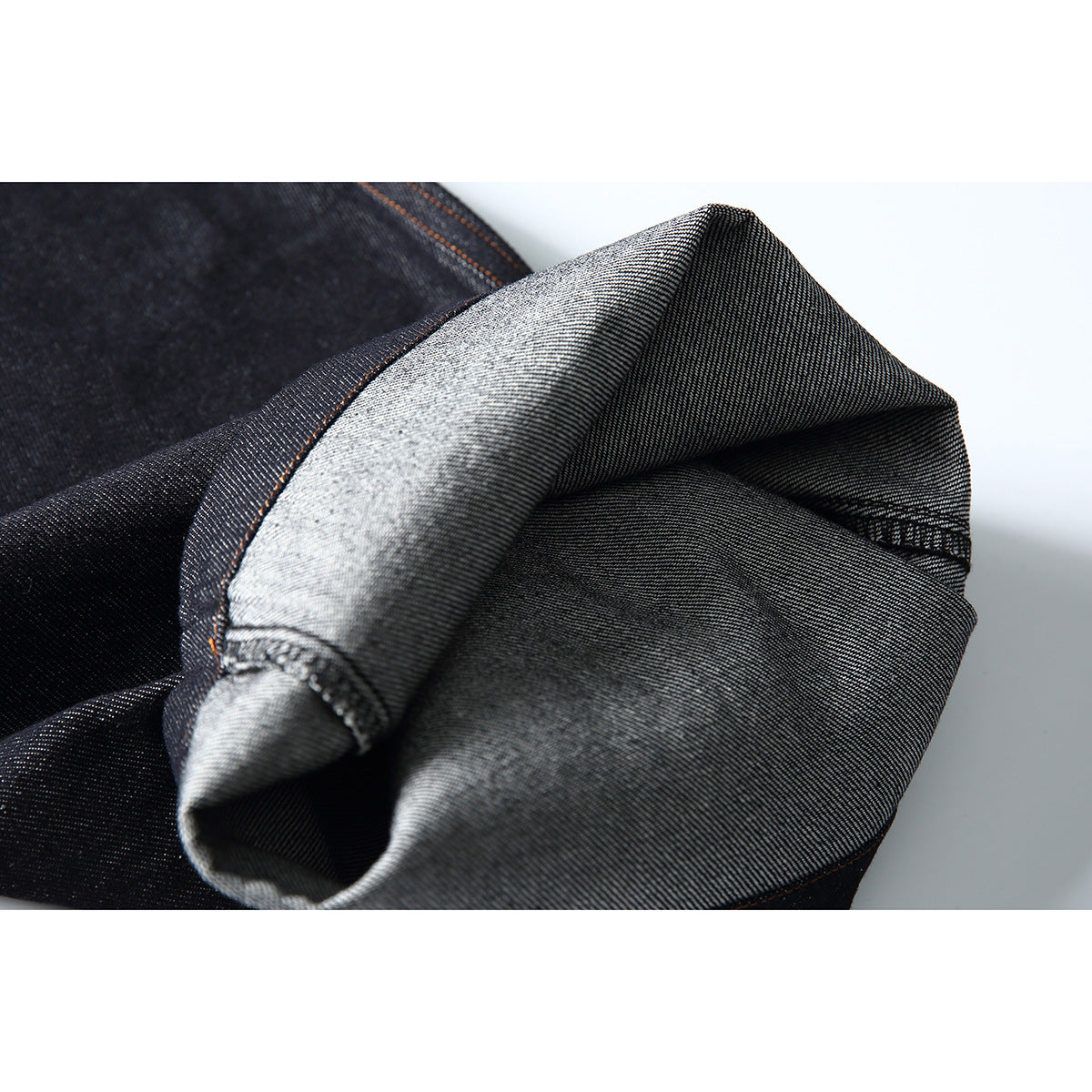 Close-up of folded dark denim revealing its lighter gray underside and stitched edge.
