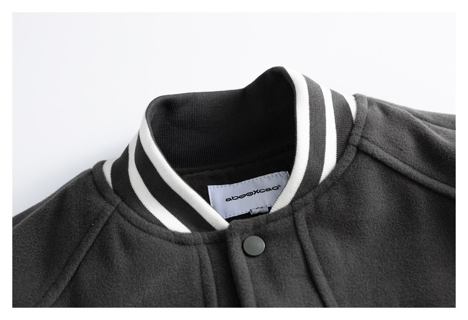 Close-up of a charcoal varsity jacket collar with black-and-white striped ribbing, a snap button, and an inner label.