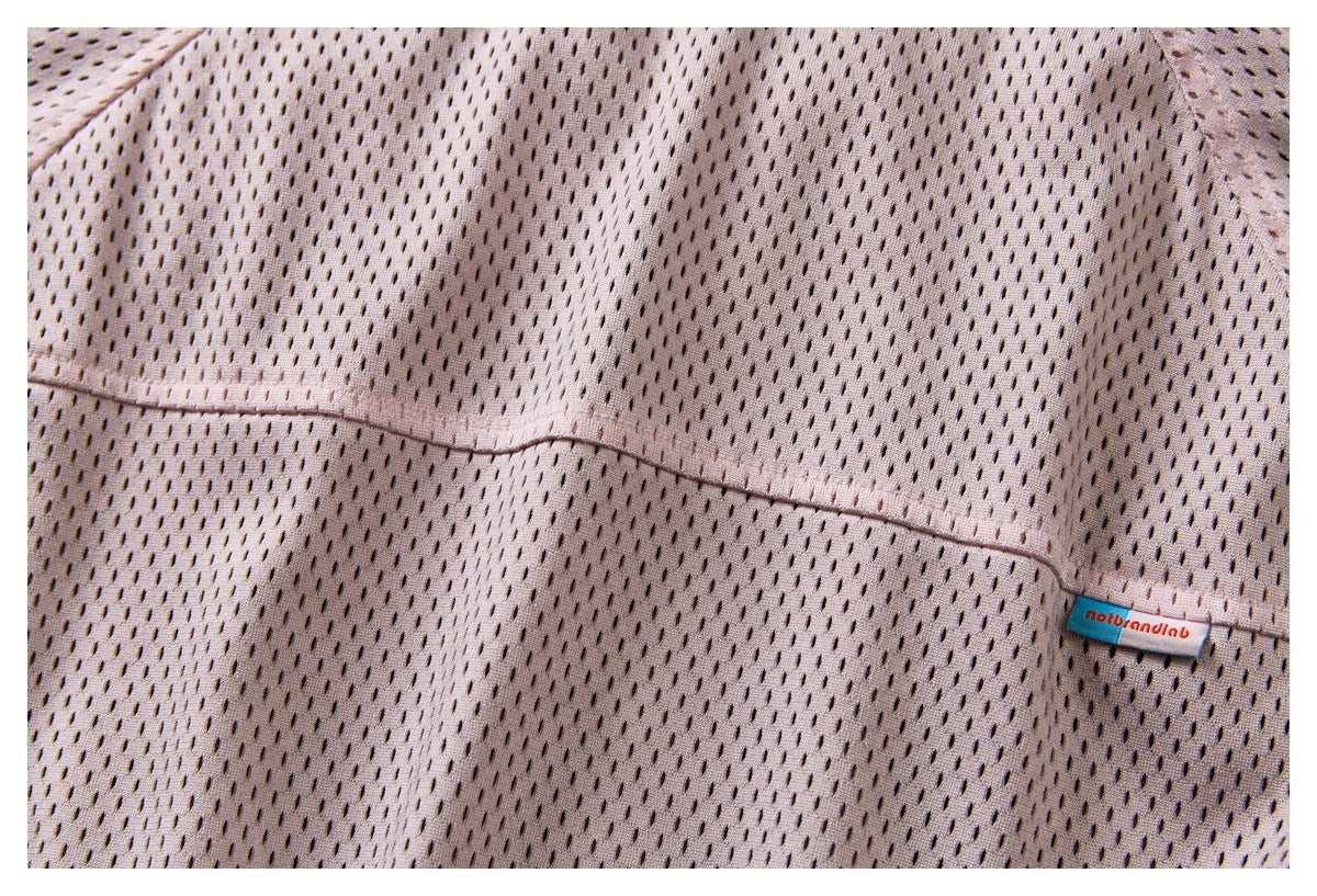 Close-up of a seam and small sewn brand label on pale mauve perforated fabric.