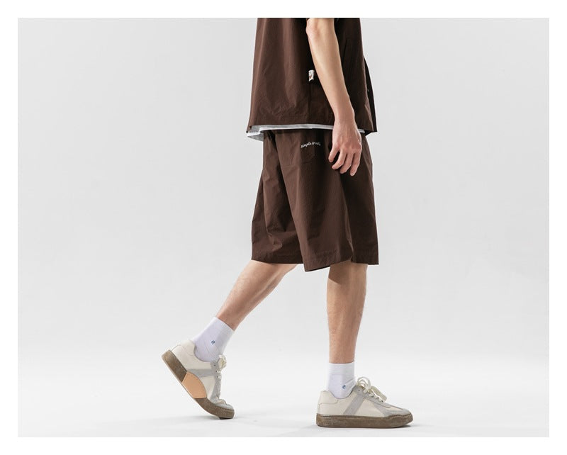 Side view of a model wearing dark brown knee-length shorts with a matching top, white socks and sneakers.