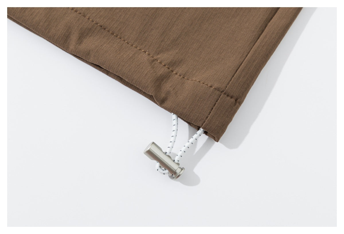 Close-up of the shirt hem with a white cord and silver toggle emerging from the brown fabric.