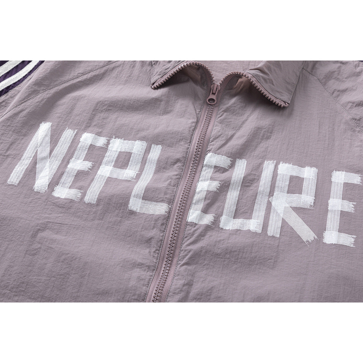 Close-up of a mauve jacket front with a central zipper and large white lettering.