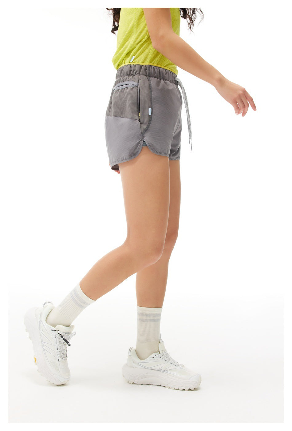 Side view of gray running shorts on a model, showing the elastic waistband, drawstring, and side pocket.