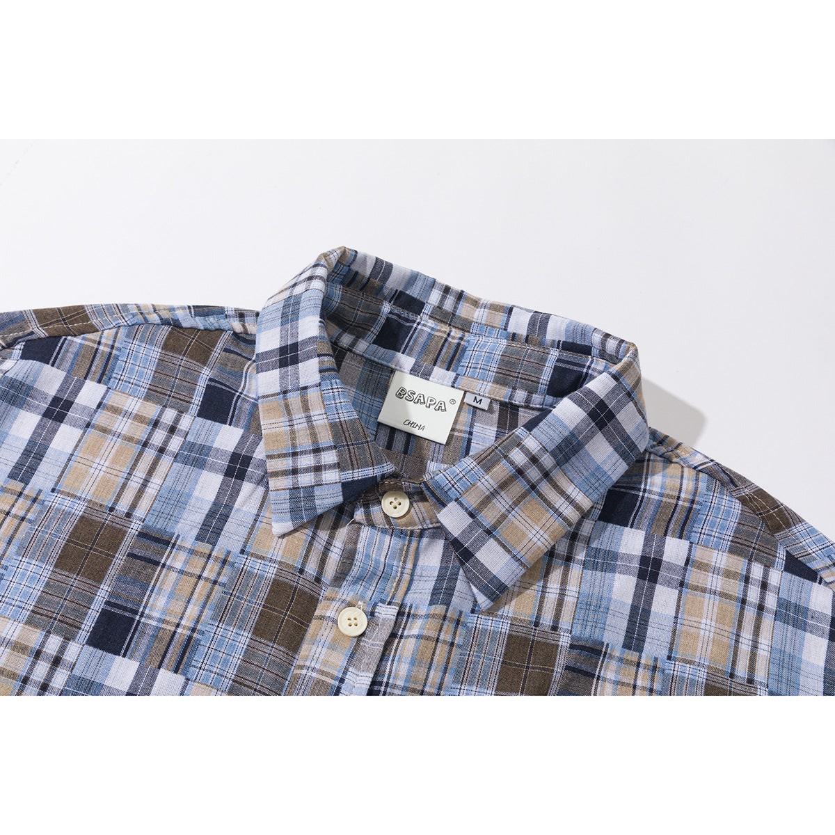 Close-up of a blue, brown, navy, and white plaid shirt collar, label, and upper button.