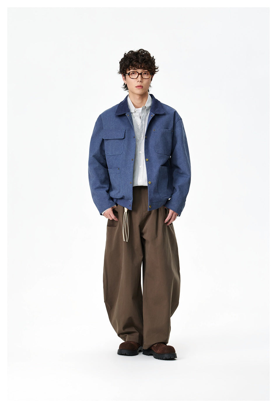 Full-length front view of a model wearing a blue utility jacket with multiple pockets and wide brown trousers.
