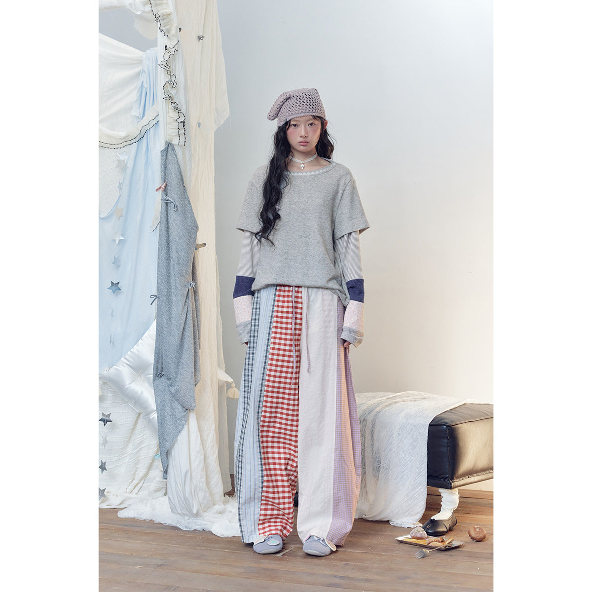 Model wearing wide patchwork trousers with red gingham, blue stripes, lilac checks and white panels.