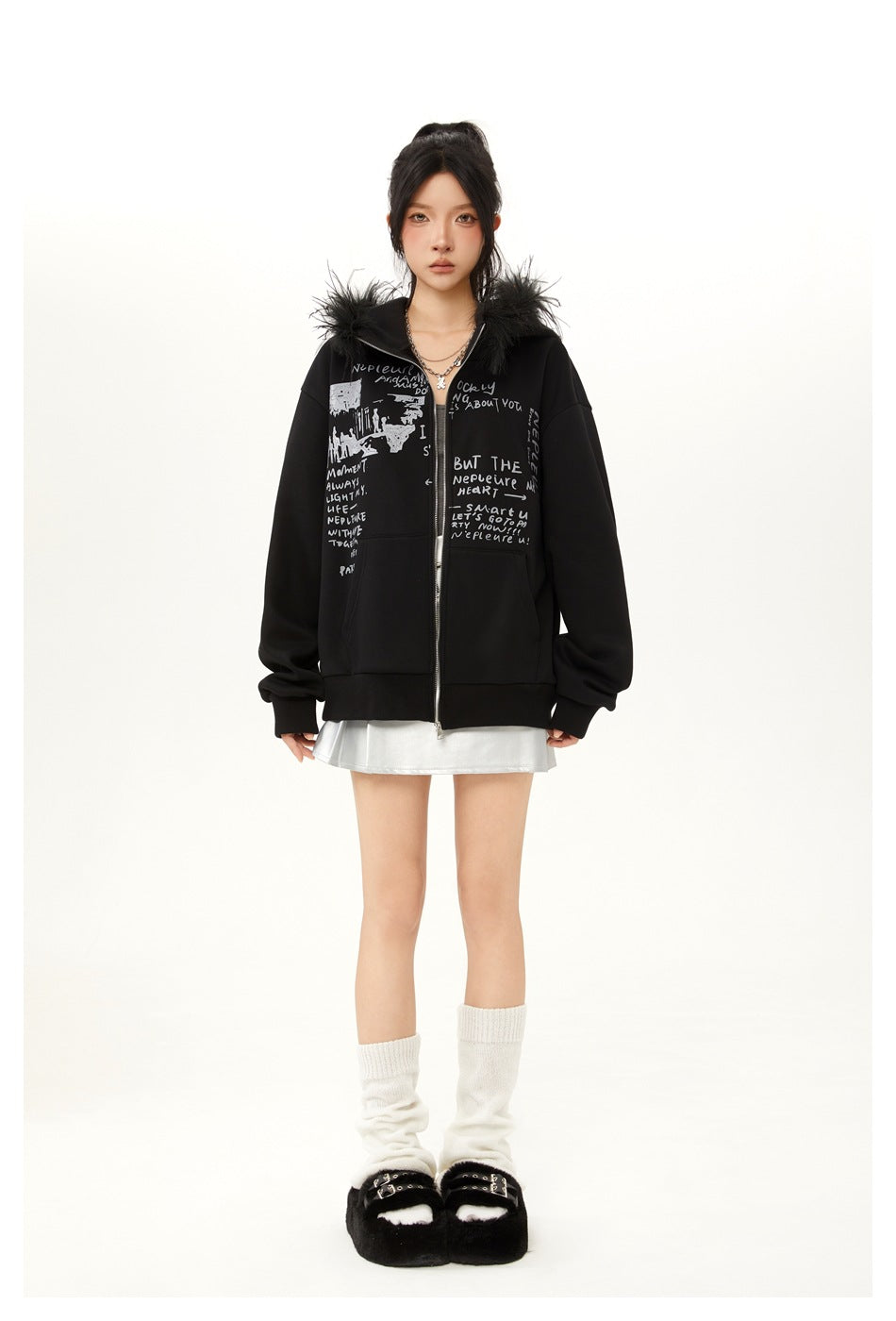 Model wearing a black oversized zip hoodie with feathery hood trim and graffiti print over a silver mini skirt