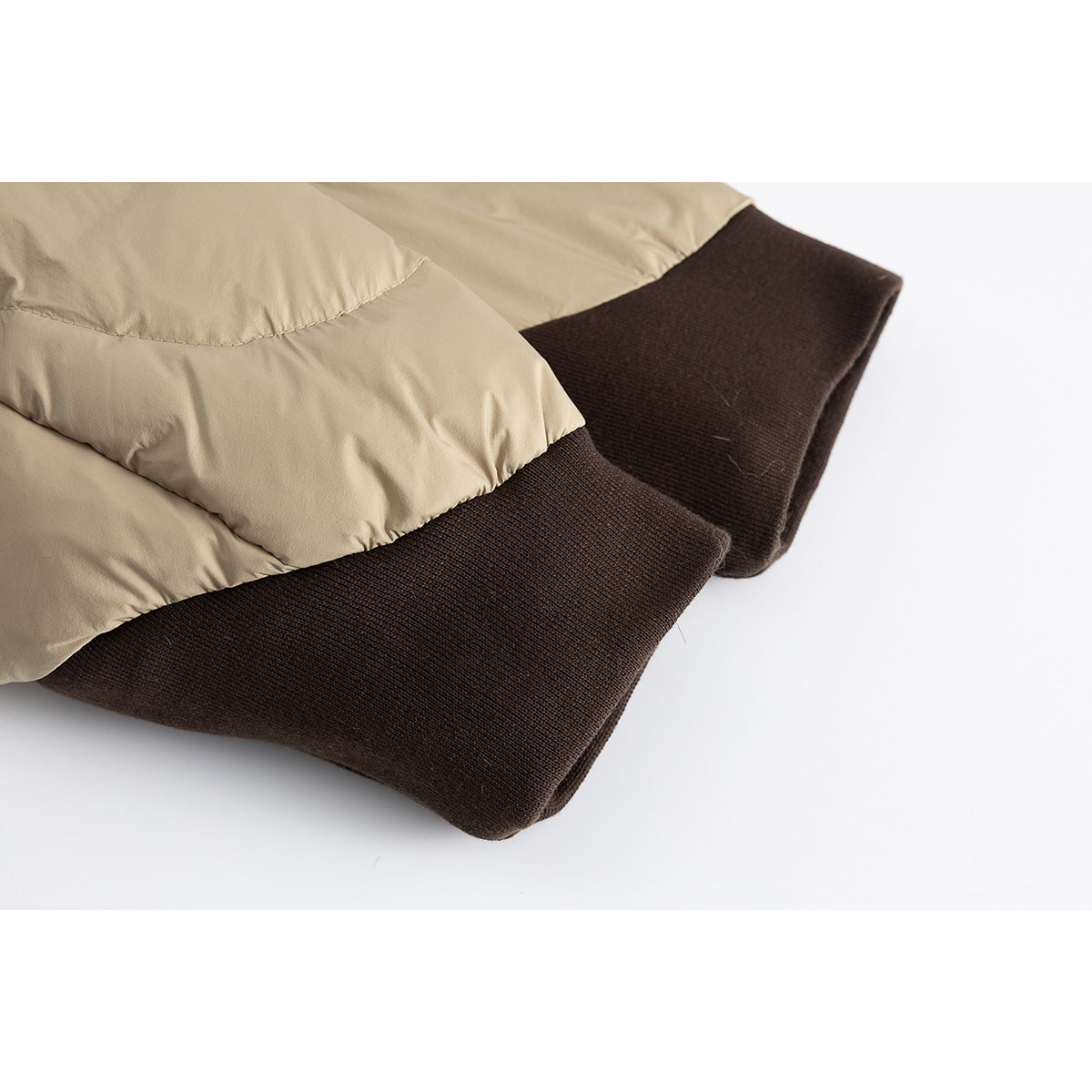 Close-up of a beige padded jacket's quilted sleeve and dark brown ribbed cuff.