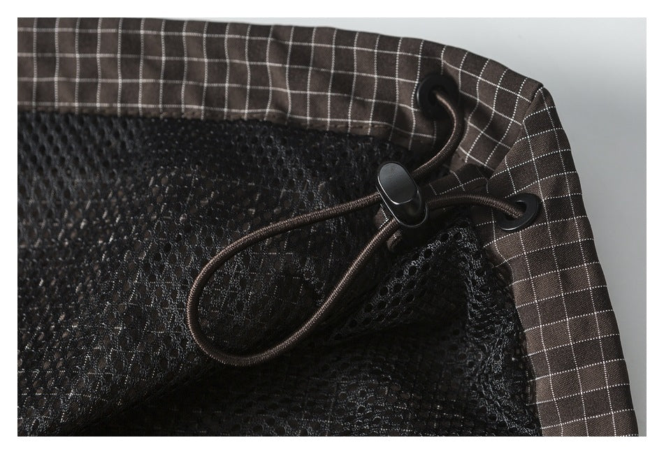 Close-up of a dark grid-patterned garment edge with black mesh lining and an adjustable drawcord.