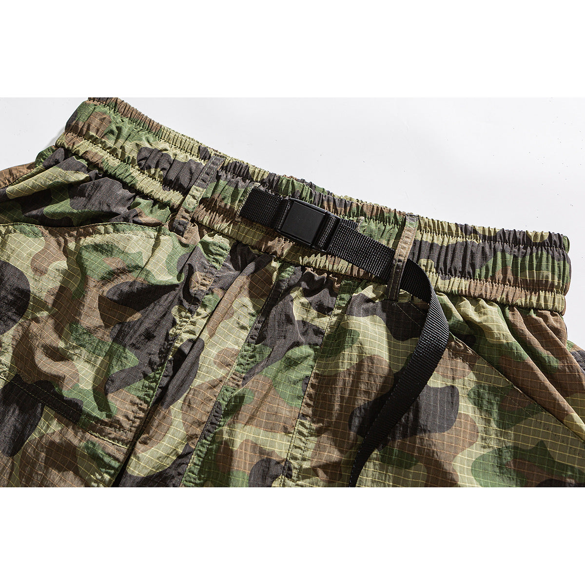 Close-up of camouflage shorts showing the gathered elastic waistband and black adjustable belt buckle.