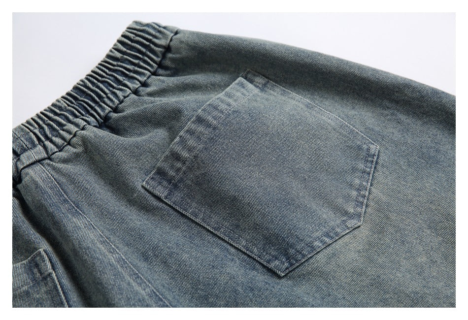 Close-up of a patch pocket and gathered elastic waistband on gray-blue denim pants.