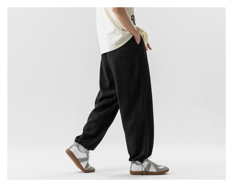 Person wearing loose black jogger pants with elastic cuffs, shown from the side with a hand in the pocket.