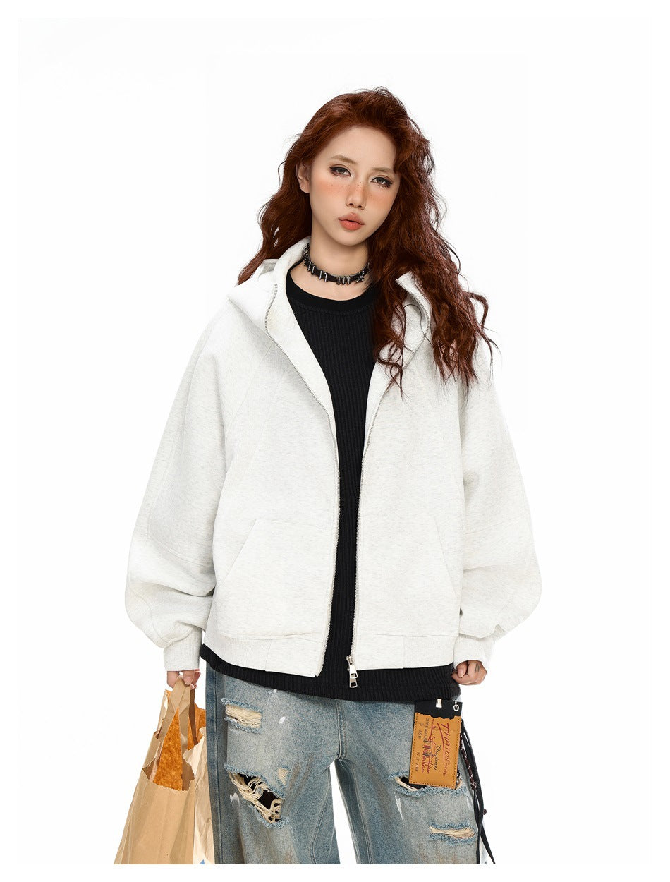 Model wearing an open light gray oversized zip hoodie over a black top, with distressed light-wash jeans.