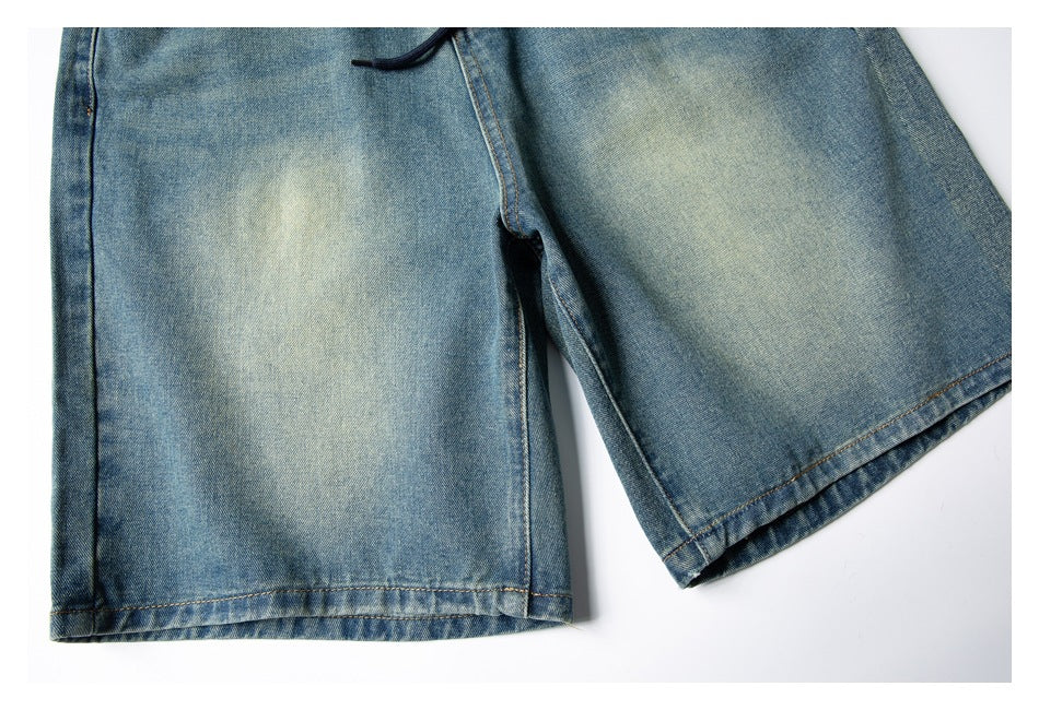 Cropped front view of faded blue denim shorts with wide legs and a dark drawstring waist.