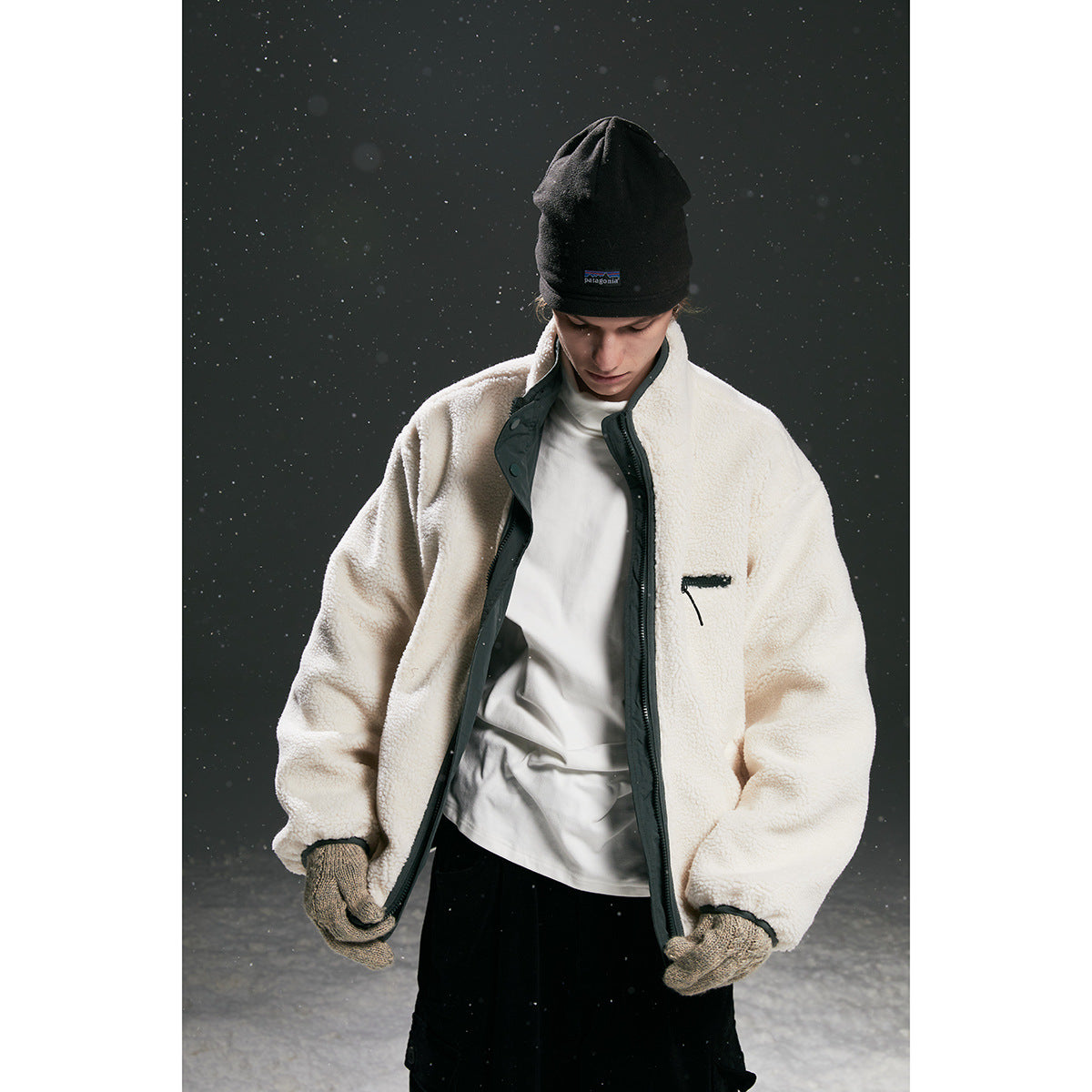 Model wearing an off-white fleece zip jacket with black trim, a black beanie and gloves.