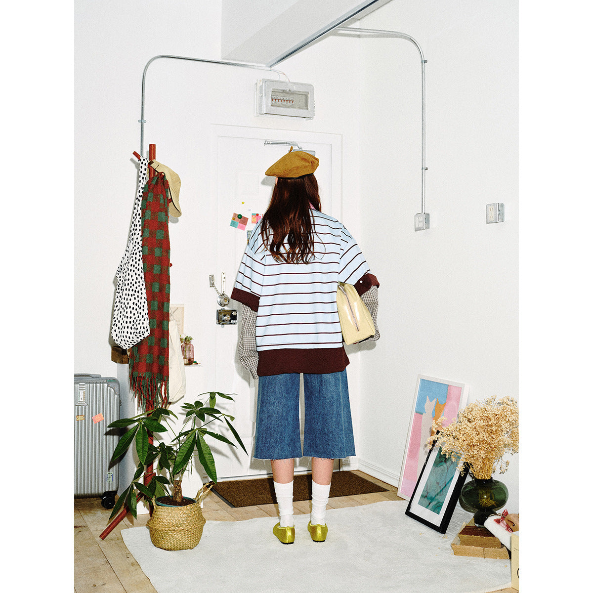 Back view of a model wearing a light blue striped top with brown trim and plaid layered sleeves, with denim culottes.